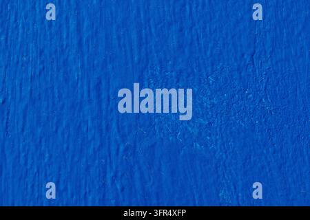 Detailed texture of a wall painted in rich blue with visible plaster grain and subtle shadows, perfect for background design and graphic overlays. Stock Photo