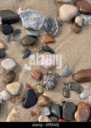 Colorful smooth pebbles and stones on wet sand at the beach, natural texture background. Stock Photo