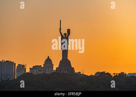 Sunset over Kyiv, Ukraine featuring a significant statue on a pedestal in an urban landscape Buildings of varying heights surround the monument Warm c Stock Photo