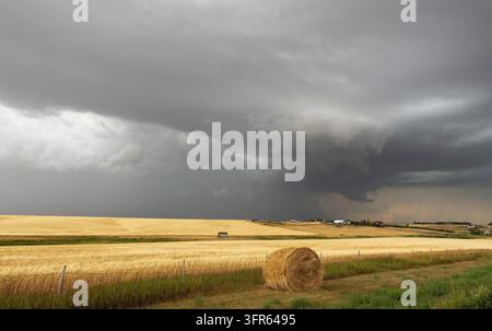 Dark storm clouds forming over a golden wheat field with hay bales, creating a dramatic and ominous scene in the countryside Stock Photo