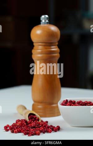Pink peppercorns in a wooden spoon with a wooden pepper shaker isolated on a black background and copy space Stock Photo