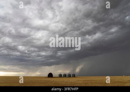 Ominous supercell storm clouds gathering over a farm with grain silos and a barn in the vast plains Stock Photo
