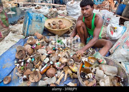 Man in green vest sits among coconut shells and old medicine bottles sorting waste near a tannery waste ground, Dhaka Division, Hazaribagh, Bangladesh Stock Photo