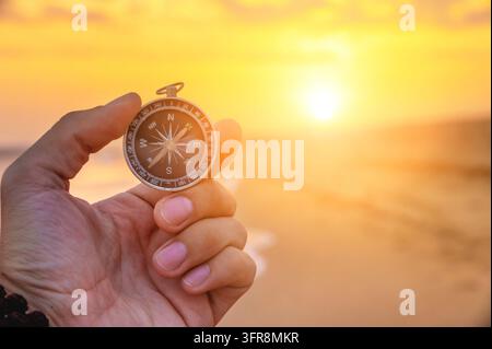 Close-up of a man's hand holding a magnetic compass against the background of the setting sun and sea Stock Photo