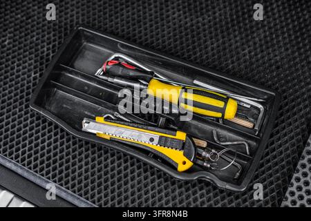 An angled view shows a black plastic tool tray holding a yellow screwdriver, utility knife, allen wrenches, and small hand tools on a rubber mat. The Stock Photo