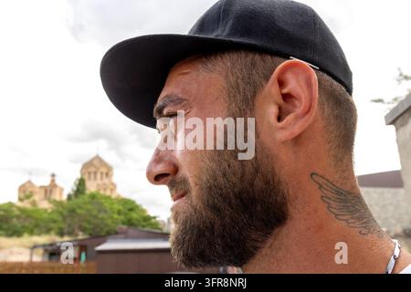 A bearded man in profile wears a baseball cap with Saint Gregory the Illuminator Cathedral visible behind him in Yerevan, Yerevan, Yerevan, Armenia Stock Photo