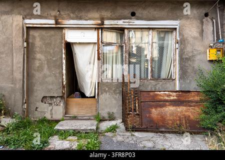 Old decayed doorway and window of a house facade with a curtain and rusty metal sheet, Yerevan, Yerevan, Armenia Stock Photo