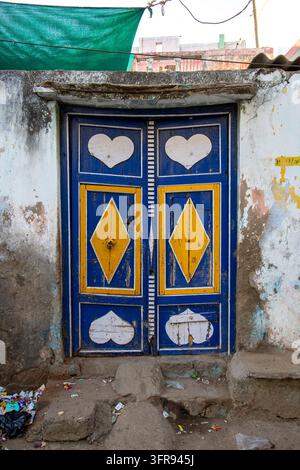A weathered wooden door painted blue and yellow is decorated with white heart motifs, Gujarat, Mandvi, India Stock Photo