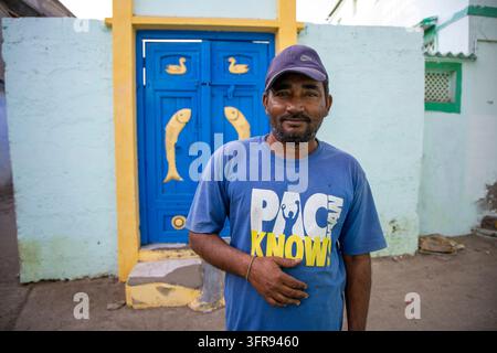 Man wearing a cap standing in front of a blue door decorated with carved fish and duck motifs, Gujarat, Mandvi, India Stock Photo