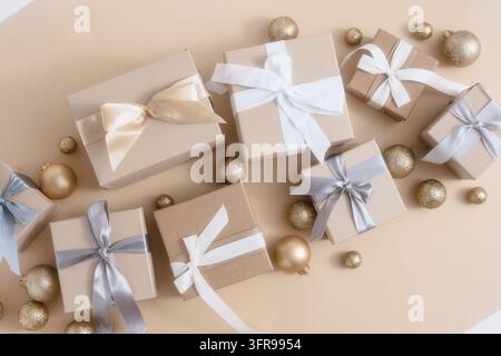 Wrapped gift boxes with white ribbons and gold baubles on beige background. Stock Photo
