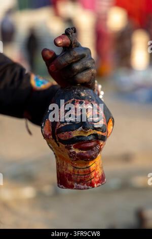 Close-up of a painted head prop held by a hand covered in black paint at Maha Kumbh Mela with a blurred background, Uttar Pradesh, Prayagraj, India Stock Photo