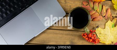 Cozy panoramic autumn workspace flat lay with laptop, cup of coffee and autumn leaves on rustic wooden table Stock Photo