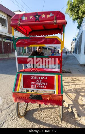 Colorful decorated rickshaw with its driver seen through the frame on a town street, Atsimo-Andrefana, Tulear, Madagascar Stock Photo