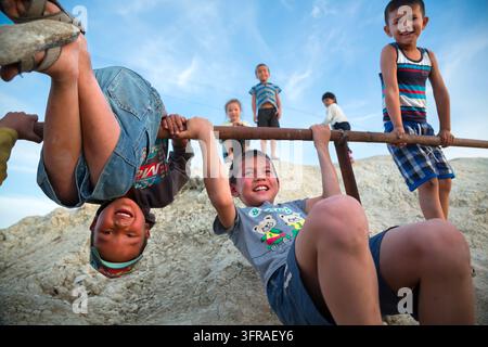 Smiling children hang from a rusty bar and look at the camera on a pale ...