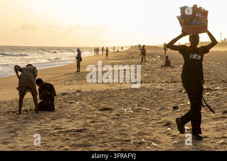 Silhouettes of people walking along a littered beach at sunset including a woman carrying a basket on her head, Maritime Region, Lome, Togo Stock Photo