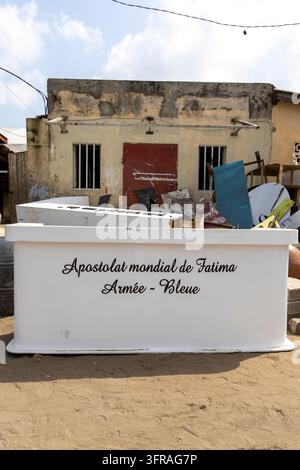 A sign for a religious association stands in front of scrap materials and an old abandoned building, Maritime Region, Lome, Togo Stock Photo