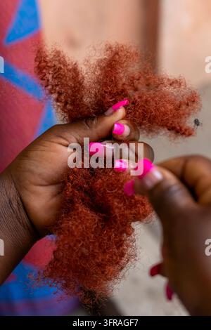 Close up of hands with pink nail polish holding reddish hair extensions, Maritime Region, Lome, Togo Stock Photo