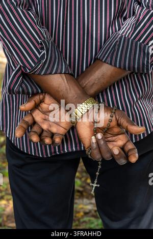 Close up of hands holding a rosary with a cross behind the back, Maritime Region, Togoville, Togo Stock Photo