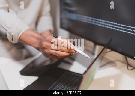Software engineer using a stylus with a tablet to review source code in a modern workspace. Close-up of programming, code debugging, software developm Stock Photo