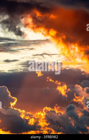 Fiery orange storm clouds illuminated by setting sun against dark dramatic evening cloudscape Stock Photo