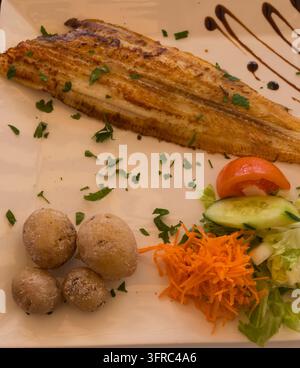 Fried plaice with canarian potatoes and vegetable salad on a plate Stock Photo