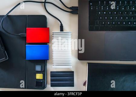 Modern Workspace Content Creator Setup External SSD Storage Hard Drive Memory Cards Laptop. Overhead top view of portable solid state drives, fast NVM Stock Photo