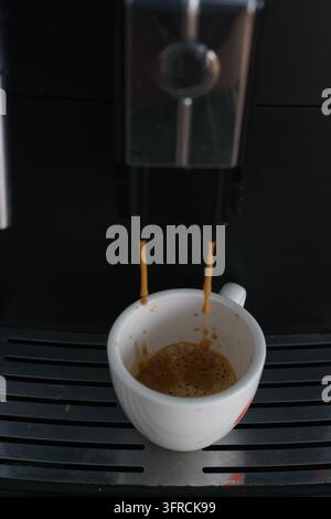 Close-up of an espresso machine dispensing coffee into a small white ceramic cup, capturing the coffee preparation process in a modern coffee machine. Stock Photo