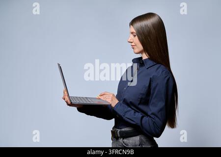 Young businesswoman working on laptop standing isolated in gray studio Stock Photo