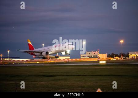 Iberia passenger aircraft descends towards the runway with landing gear extended and landing lights illuminated at dusk. Stock Photo