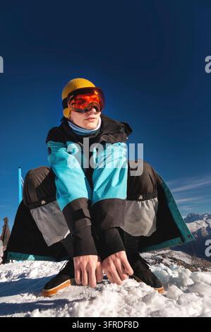 Man sitting on top of a hill. Young man squatting in warm clothes on a sunny day in the snowy mountains Stock Photo