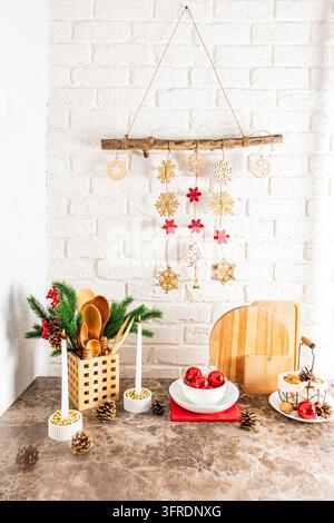A bouquet of spruce branches, burning candles, red balls and a handmade garland on a white brick wall in the interior of a modern kitchen Stock Photo