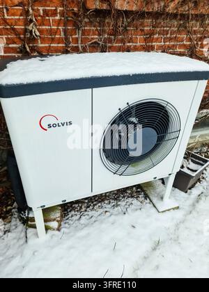 Kiel, Germany - 25 January 2025: White SOLVIS heat pump installed outside a house, working during winter with snow covering it, near a brick wall Stock Photo