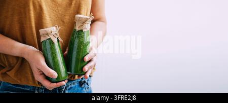 Female hands hold bottles of freshly made green smoothie, selective focus, copy space. Vegetarianism healthy lifestyle. Small business concept, produc Stock Photo