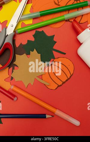 Close up of colorful autumn paper leaves and cutout pumpkins, accompanied by scissors, glue, and markers, autumn crafts concept Stock Photo