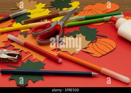 Close up from a low angle of colorful autumn paper leaves, cutout pumpkins, and creative materials on a table, autumn crafts concept Stock Photo