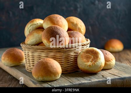 Basket with freshly baked golden crust buns on a wooden shelf, selective focus. Concept of home baking Stock Photo