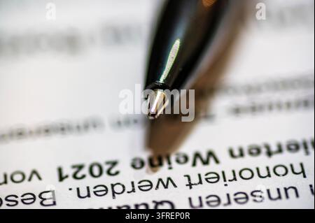 Macro photograph of a black ballpoint pen tip hovering above a printed document with German text. The image has shallow depth of field, focusing sharp Stock Photo