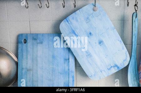 Close-up of two wooden cutting boards hanging on a tiled wall on metal hooks, blue toned Stock Photo