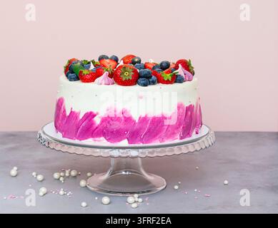 Delicate cake decorated with fresh berries, strawberries and blueberries on a light plain background. Festive dessert with berries on a glass plate st Stock Photo