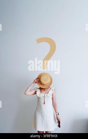 Woman in a summer dress beneath a question mark, visualizing uncertainty, choice and travel planning for decision-making campaigns. Stock Photo