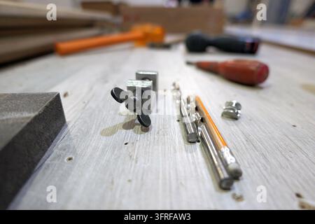 Various essential tools for carpentry and diy projects, including a clamp, drill bits, pencil, and sandpaper, lying on a light wooden workbench, signi Stock Photo