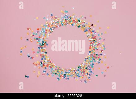 Sequins multicolored confetti lined in a round frame pink background. Abstract festive composition place for text Stock Photo