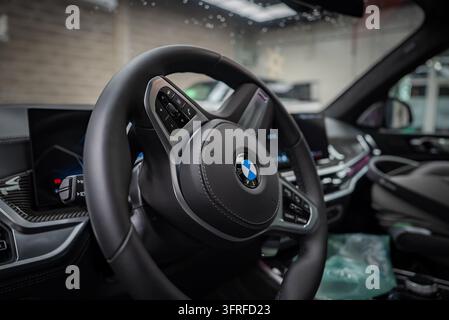 Steering wheel and modern dashboard interior of a luxury BMW X7 parked inside an underground auto detailing workshop. Leather stitched controls and di Stock Photo