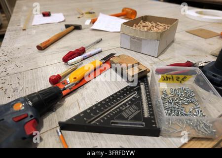 Woodworking tools and carpentry supplies  drill, screws, dowels, speed square and utility knife  arranged on a dusty workbench suggesting an ongoing d Stock Photo