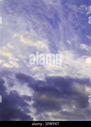 Sky filled with soft white clouds against deep blue background. Darker clouds gather at bottom. Cloud formations suggest calm, transitional weather. C Stock Photo