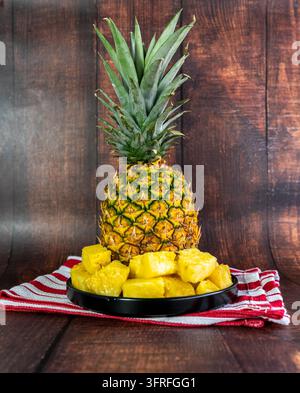 Fresh pineapple chunks served on a black plate with a whole ripe tropical pineapple softly blurred in the background. Stock Photo