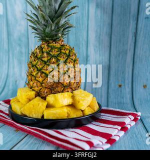 Fresh pineapple chunks served on a black plate with a whole ripe tropical pineapple softly blurred in the background. Stock Photo
