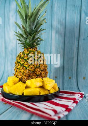 Fresh pineapple chunks served on a black plate with a whole ripe tropical pineapple softly blurred in the background. Stock Photo