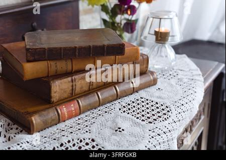 Stack of antique leather-bound books on a white crocheted lace runner, with flowers and a lit candle in a glass holder in the background. Stock Photo