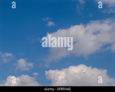 Blue sky with fluffy white clouds. Clouds float gently across clear blue background. Bright, open sky with soft, cotton-like cloud formations Stock Photo